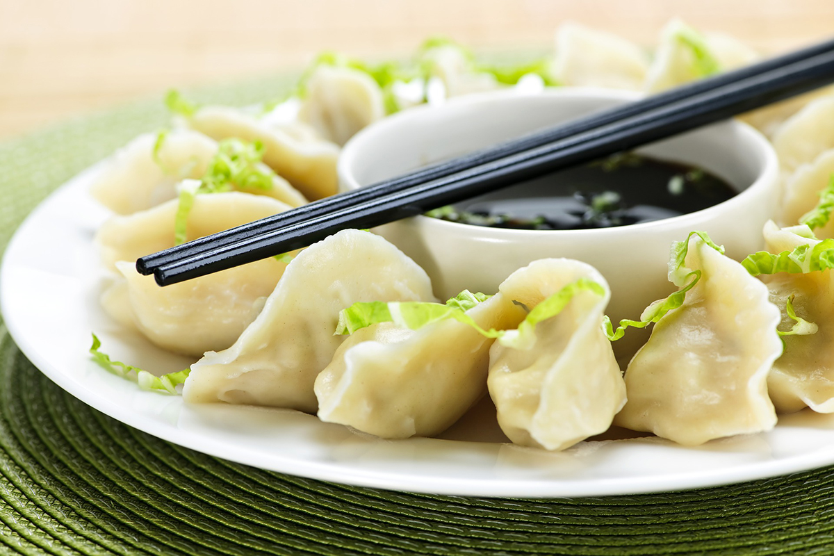 Steamed dumplings served with dark dipping sauce and black chopsticks